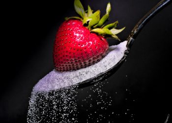 Sugar spilling from spoon with strawberry